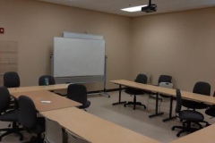 A picture of a classroom with a whiteboard and tables and chairs. 
